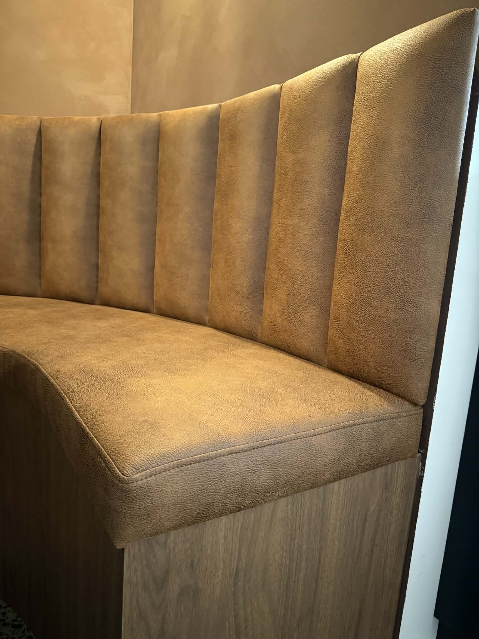 Close-up of the channel-stitched backrest meeting the seat cushion above the walnut base