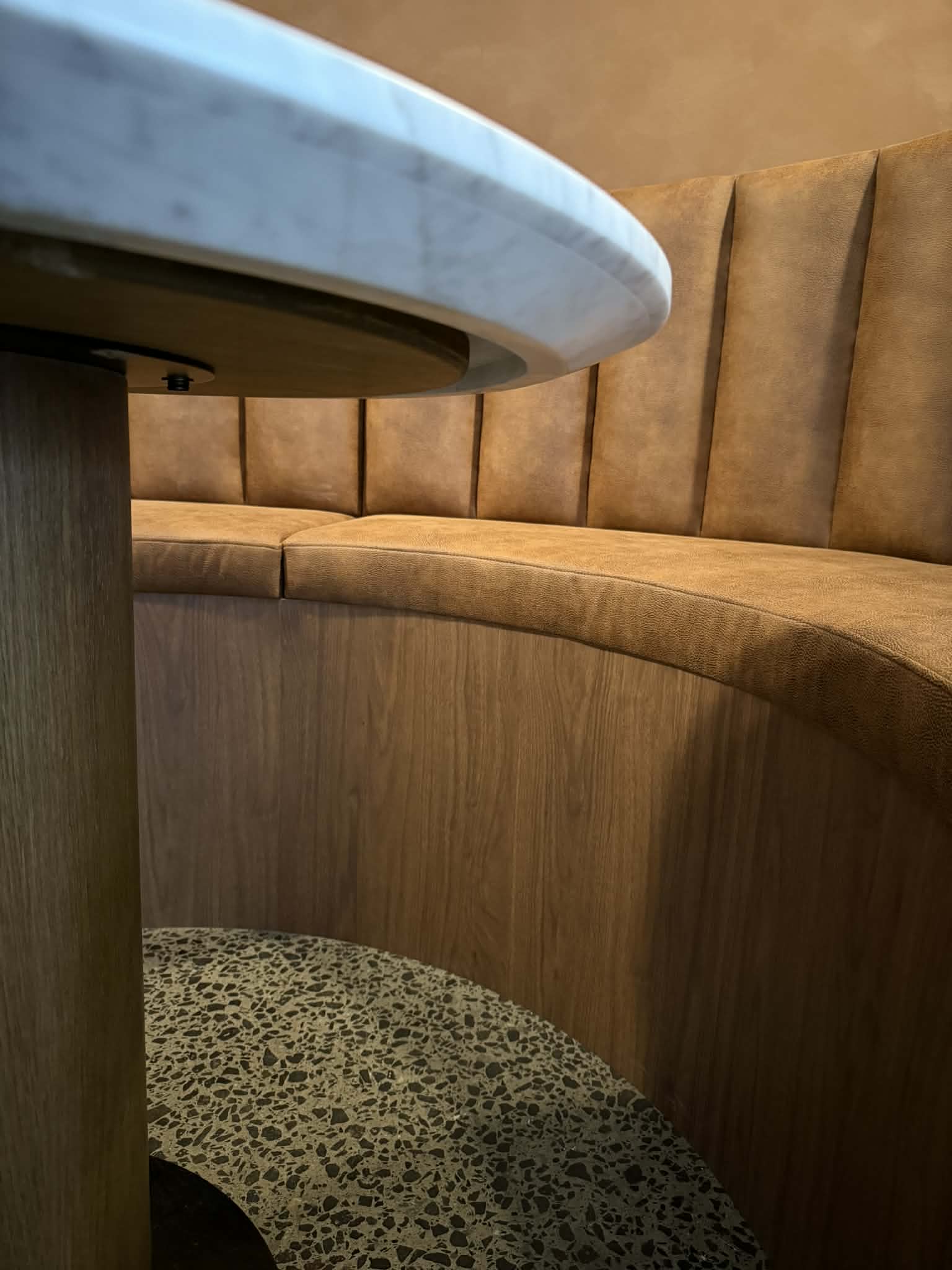 The curved walnut base panel following the sweep of the seat, under the marble tabletop