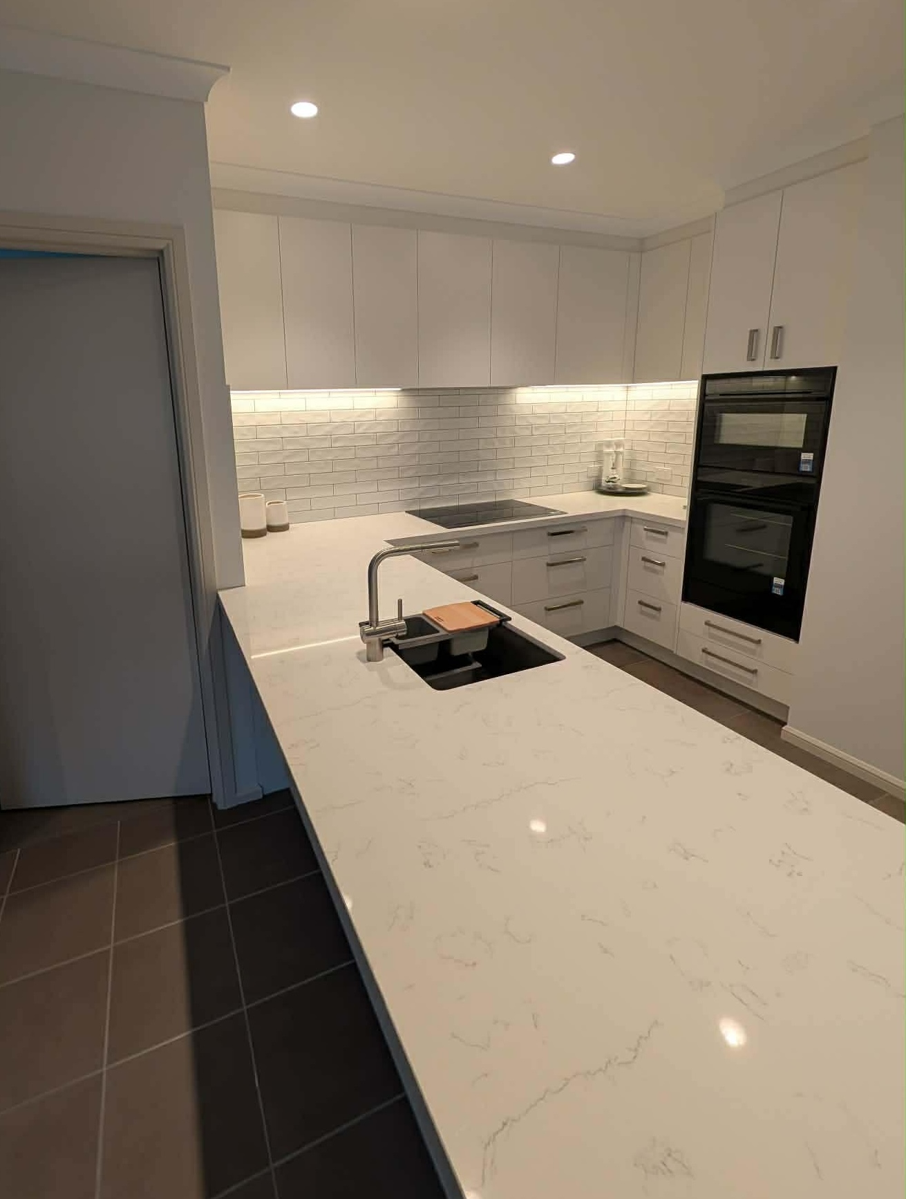 Mornington kitchen in Blossom White with a Kalala Bianco stone benchtop, black wall ovens and a white subway splashback