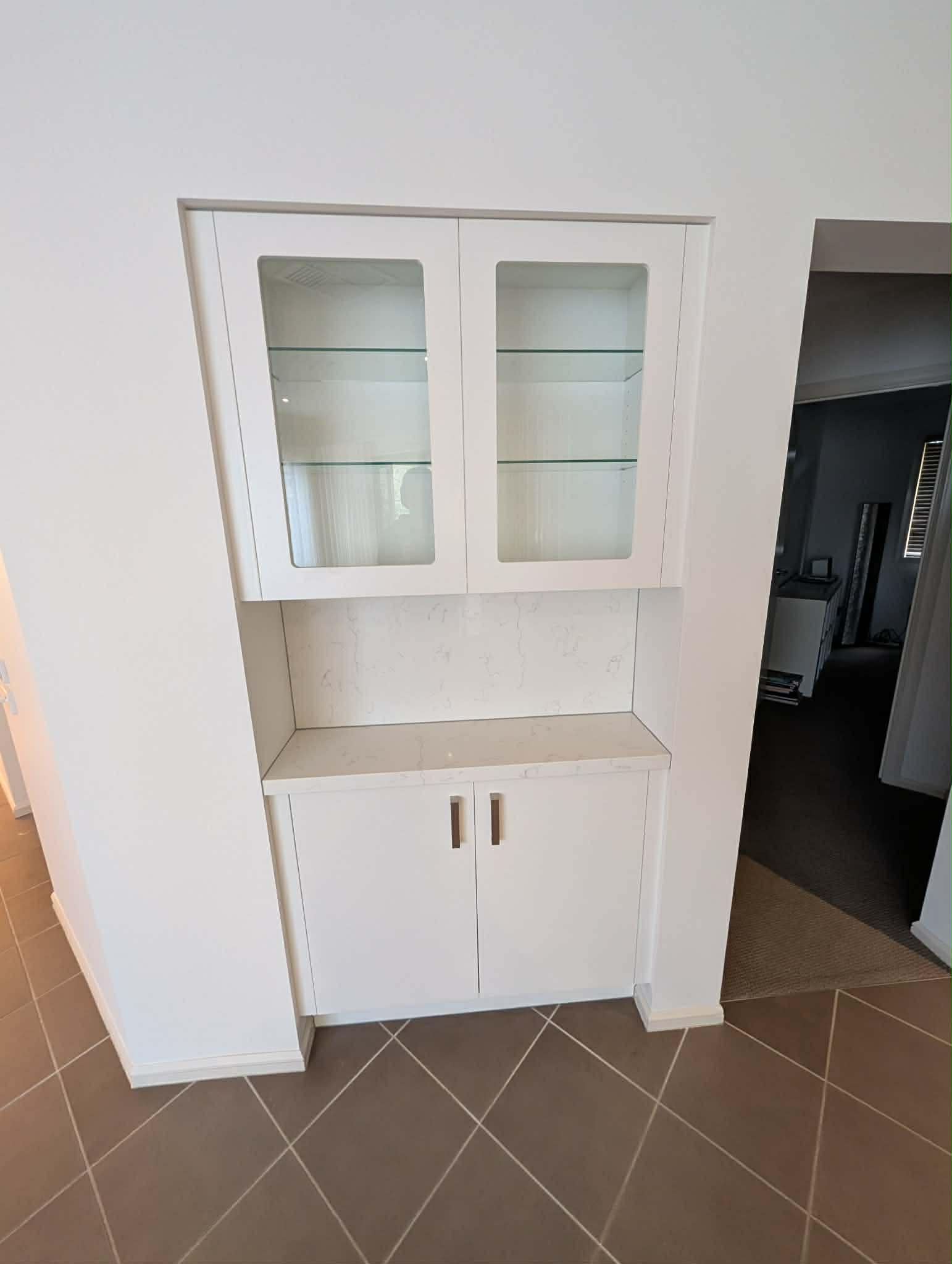 Built-in display cabinet with glass doors and glass shelves over a stone-topped cupboard