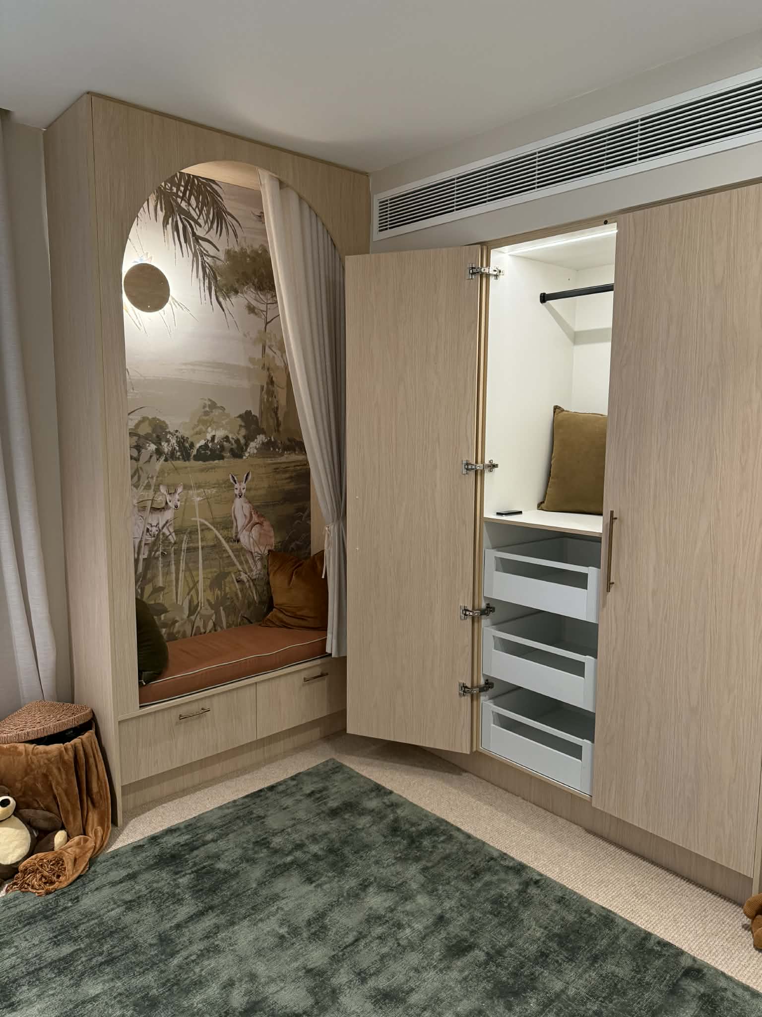 Kids' bedroom with an arched reading nook and a wardrobe in Polytec Blonde Oak Woodmatt, the wardrobe open to show lit hanging space and drawers
