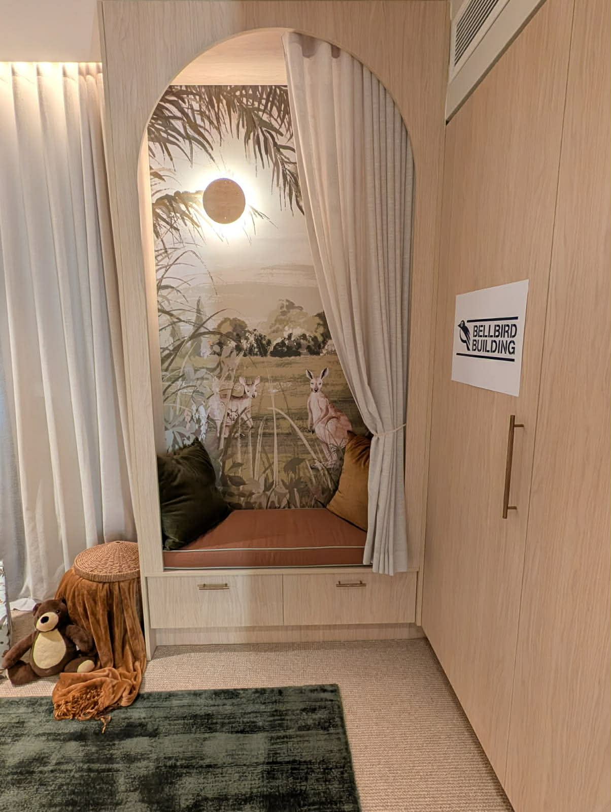 The arched reading nook framing a bushland mural, with a cushioned seat over two drawers and a Bellbird Building sign on the wardrobe beside it