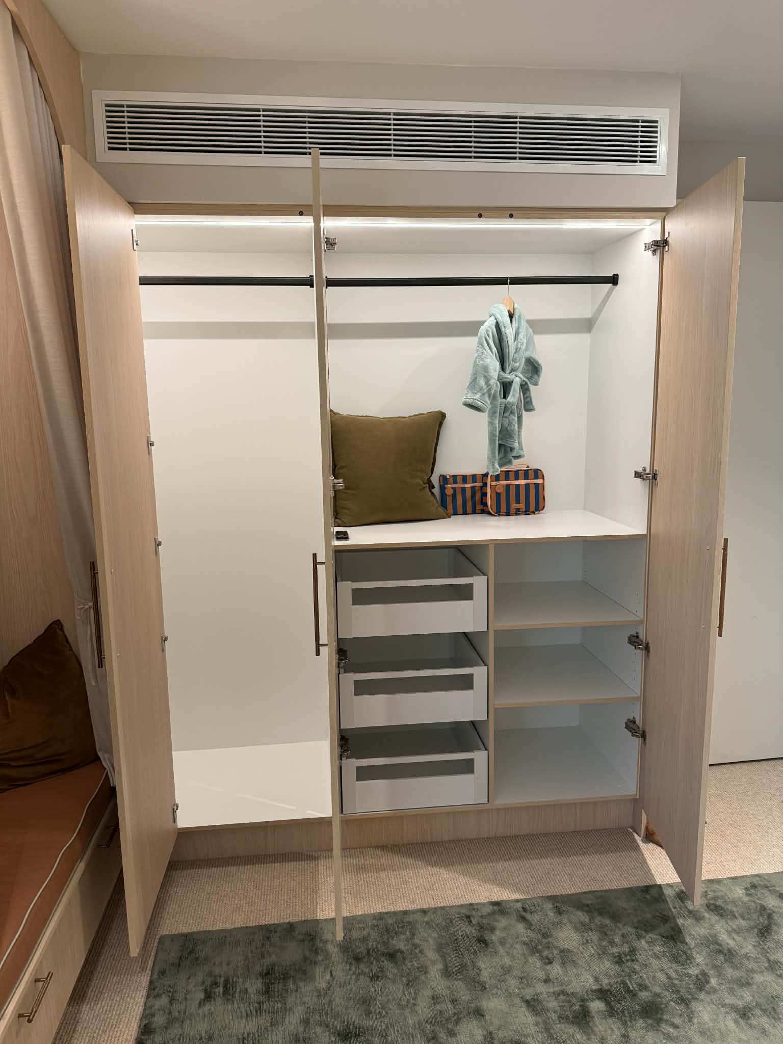 The wardrobe with both doors open: a lit hanging rail across the top, a bank of drawers and open shelves below