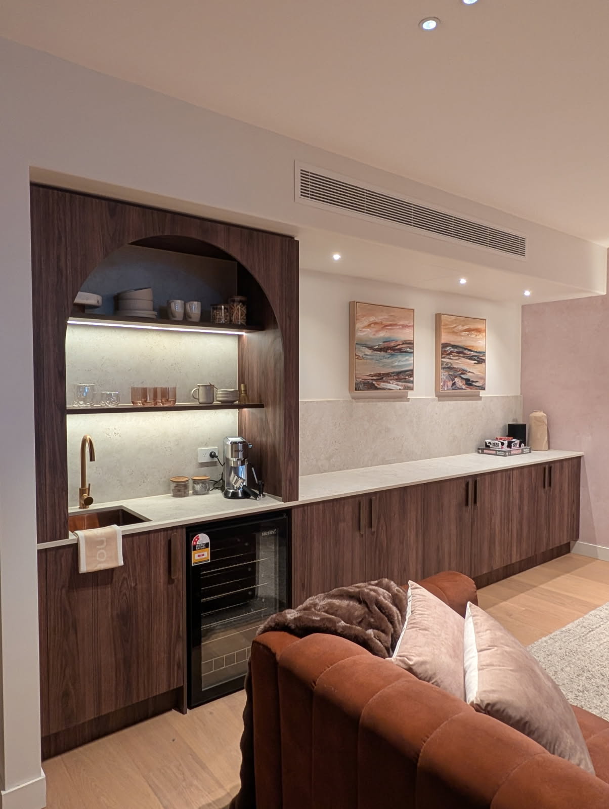 Rumpus-room kitchenette in Polytec Rojo Walnut, with an arched open-shelf niche over a sink and wine fridge and a long run of cupboards beyond