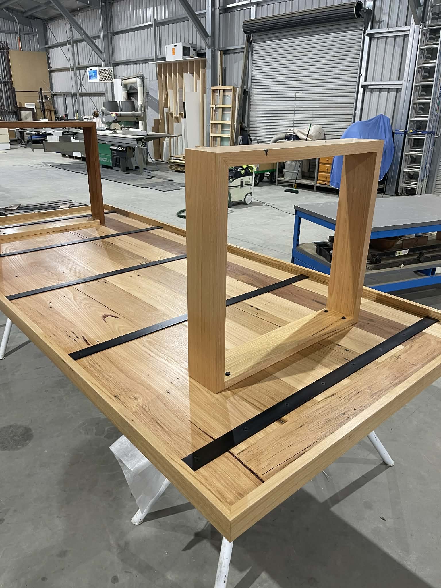 A recycled timber dining table on the bench in the Somerville workshop, base frame sitting upended on the top